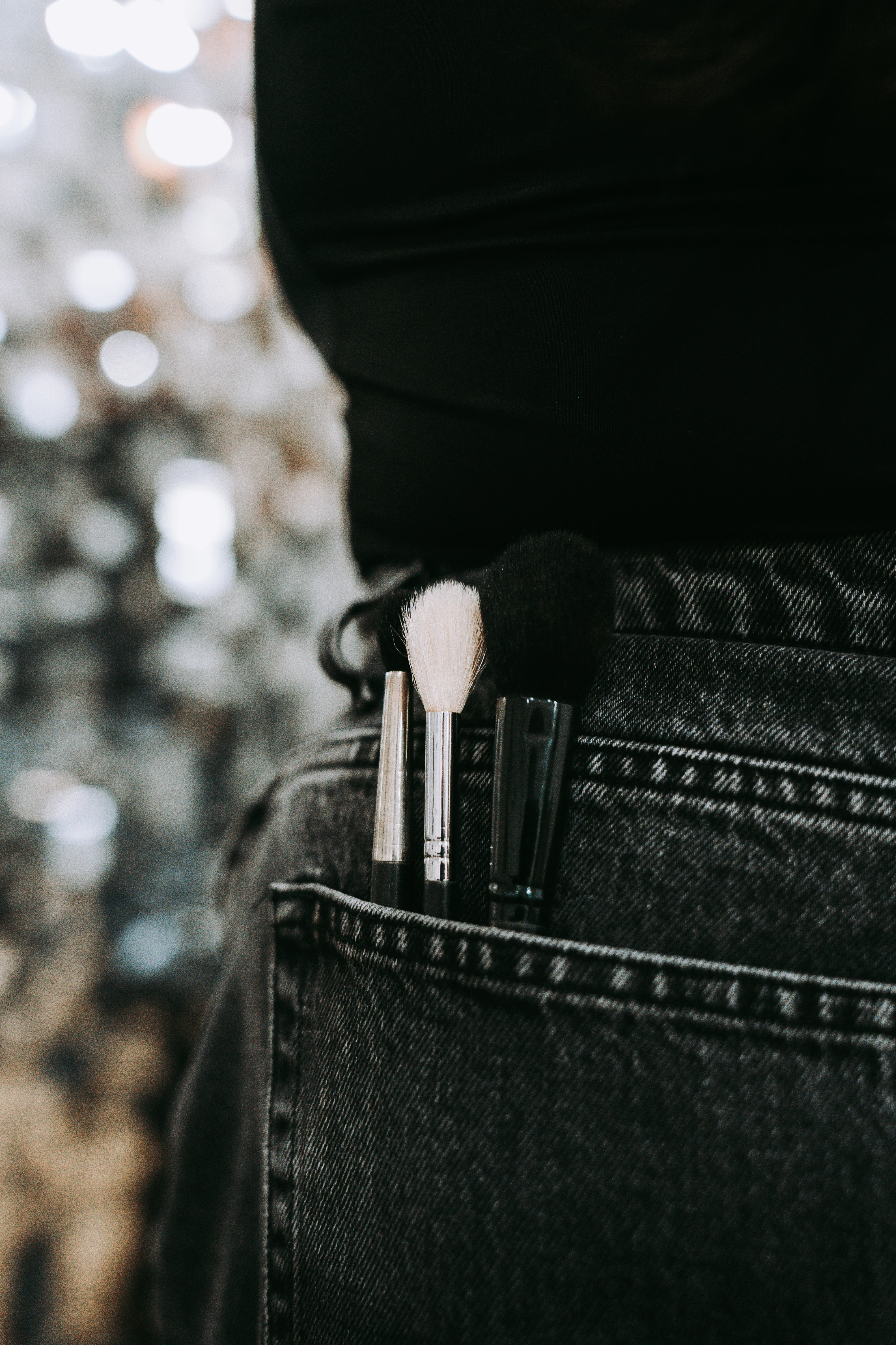 Makeup brushes tucked into a back pocket with sparkling bokeh lights