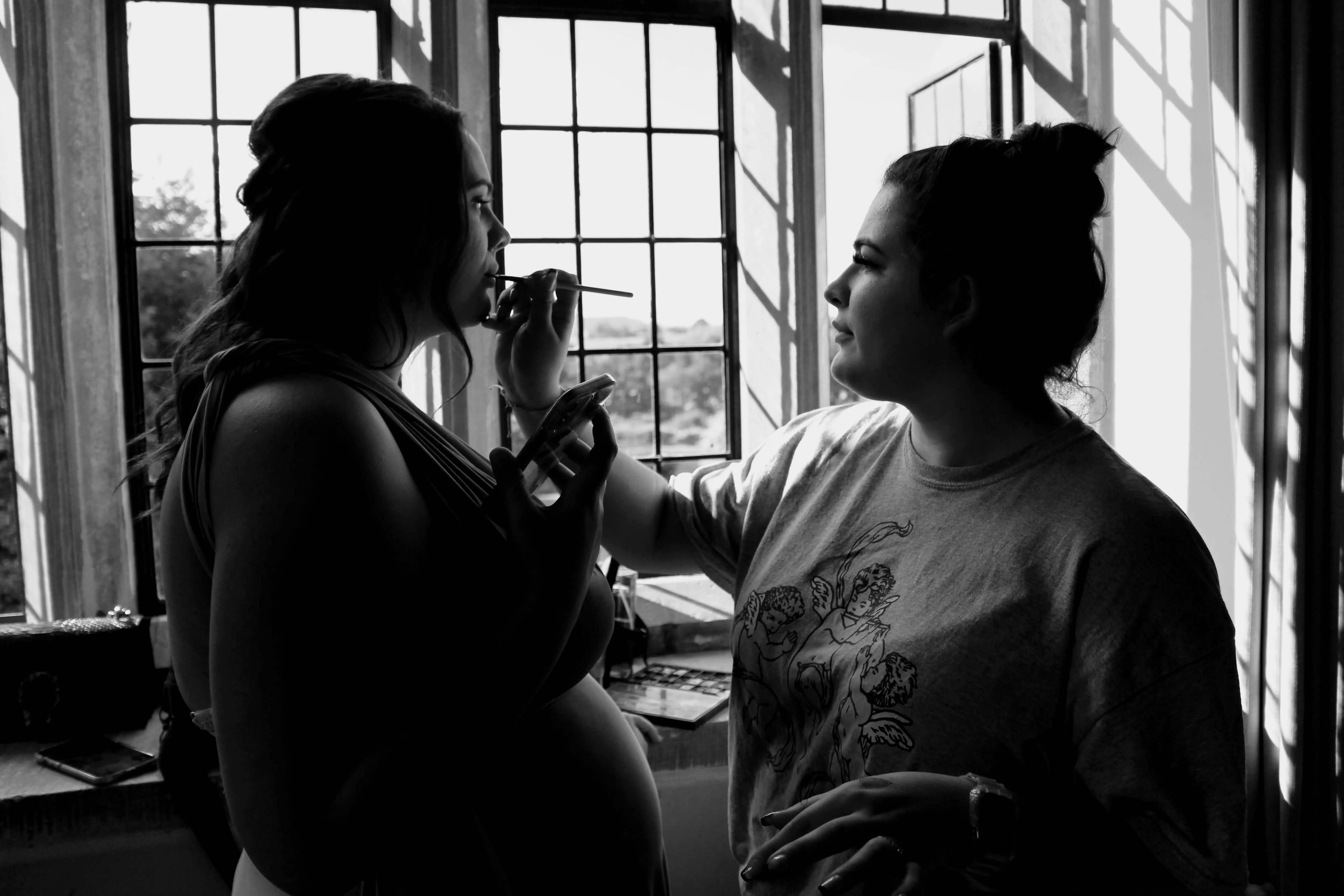 Makeup artist applying bridal makeup by a window