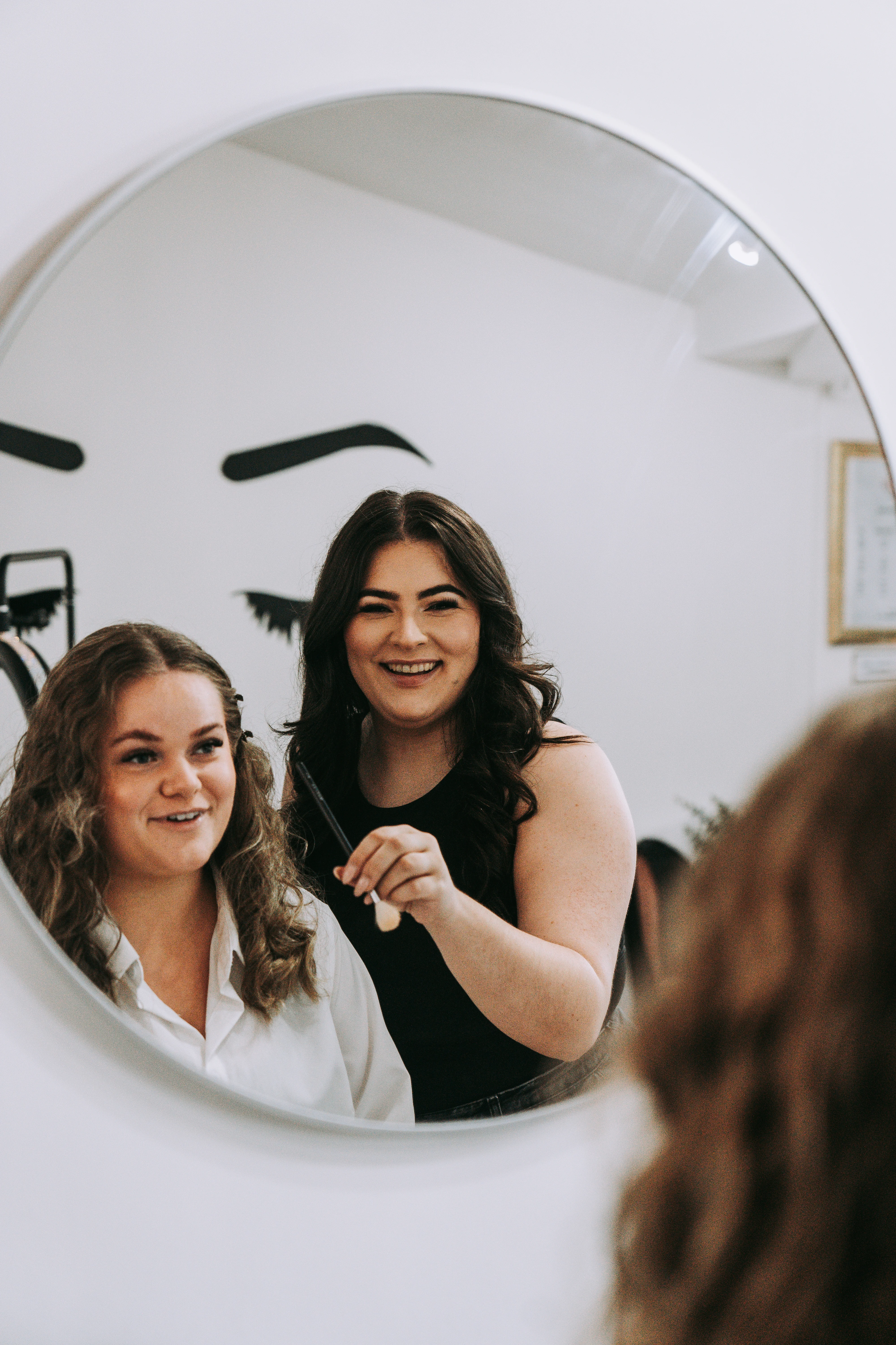 Jade laughing with a client reflected in a round mirror during styling